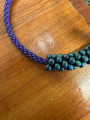 Beaded bracelet section with green beads and purple cord on a wooden surface