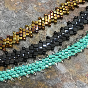 Three beaded bracelets in gold, black, and turquoise on a stone surface