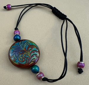 Adjustable bracelet with a round, multicolored focal bead and beads on a beige background